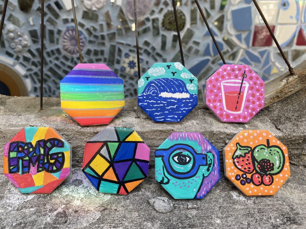 7 colorful octagon magnets leaning against a bicycle wheel with mosaic in the background