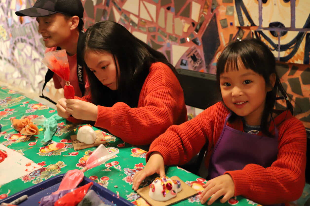 Three people sitting at a table making sugar skulls