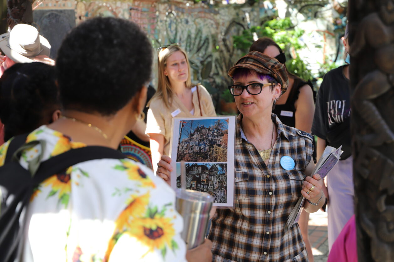 A woman tour guide holds up a visual aid to a tour group in the outdoor area of Philadelphia's Magic Gardens.